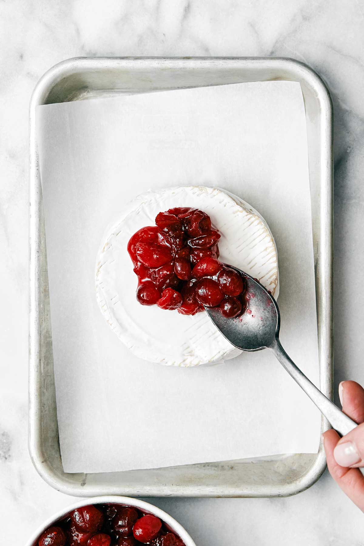 The most perfect baked brie with cranberry sauce for a festive, holiday appetizer! Plus, it's made in under 10 minutes. Adding a spoonful of cranberry sauce on brie.