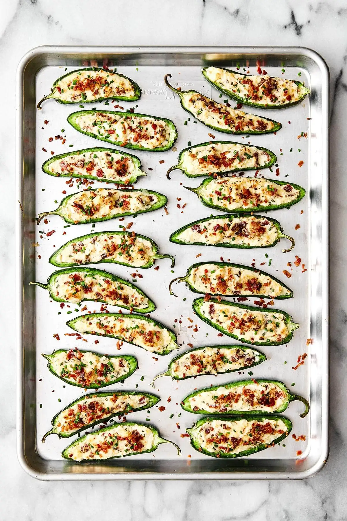 These jalapeño poppers are the ultimate party appetizer—especially for game day! They're cheesy, savory, and dotted with crispy bacon. Baked jalapeño poppers on a sheet pan.