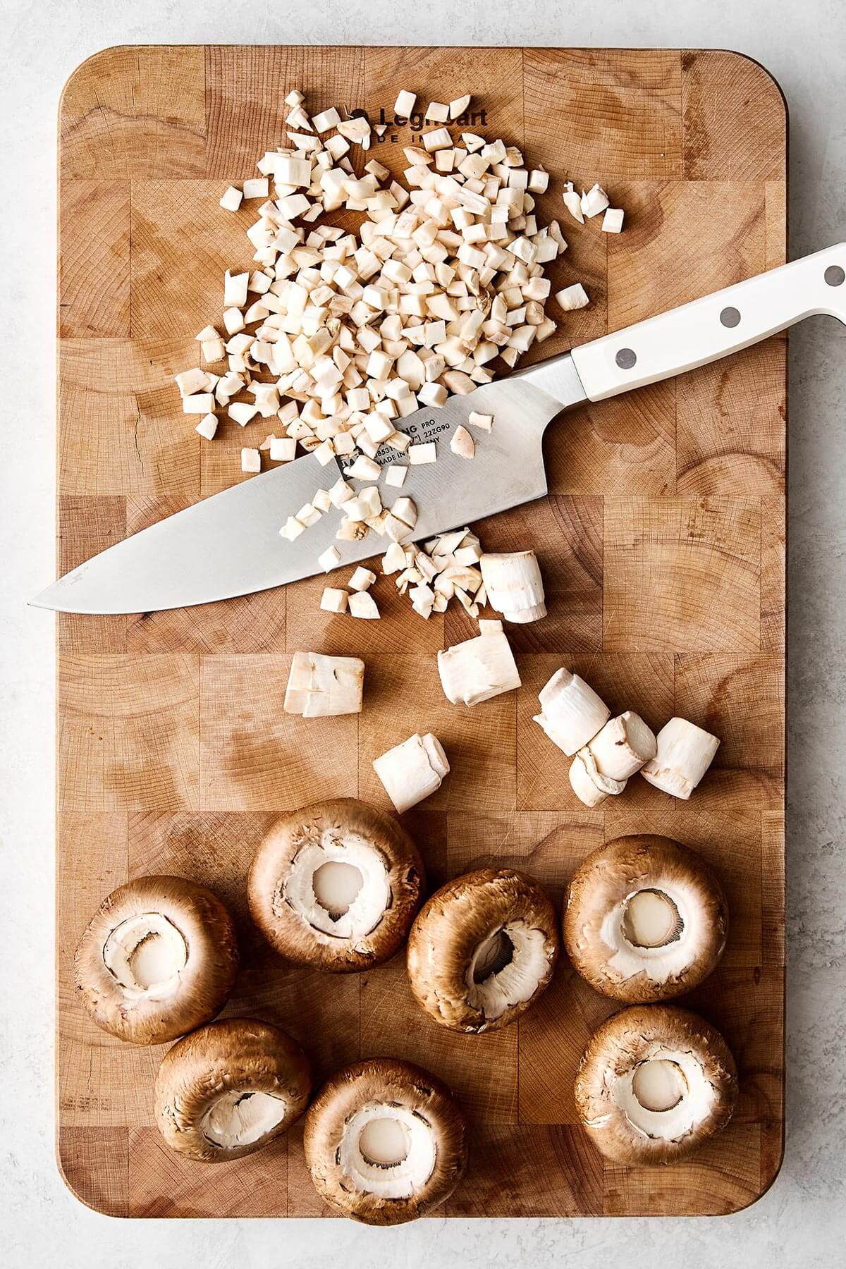 Stuffed mushrooms are always a holiday favorite! They're the perfect cheesy mushroom bite with hints of onion, herbs, and pecans. Dicing mushrooms on a board.