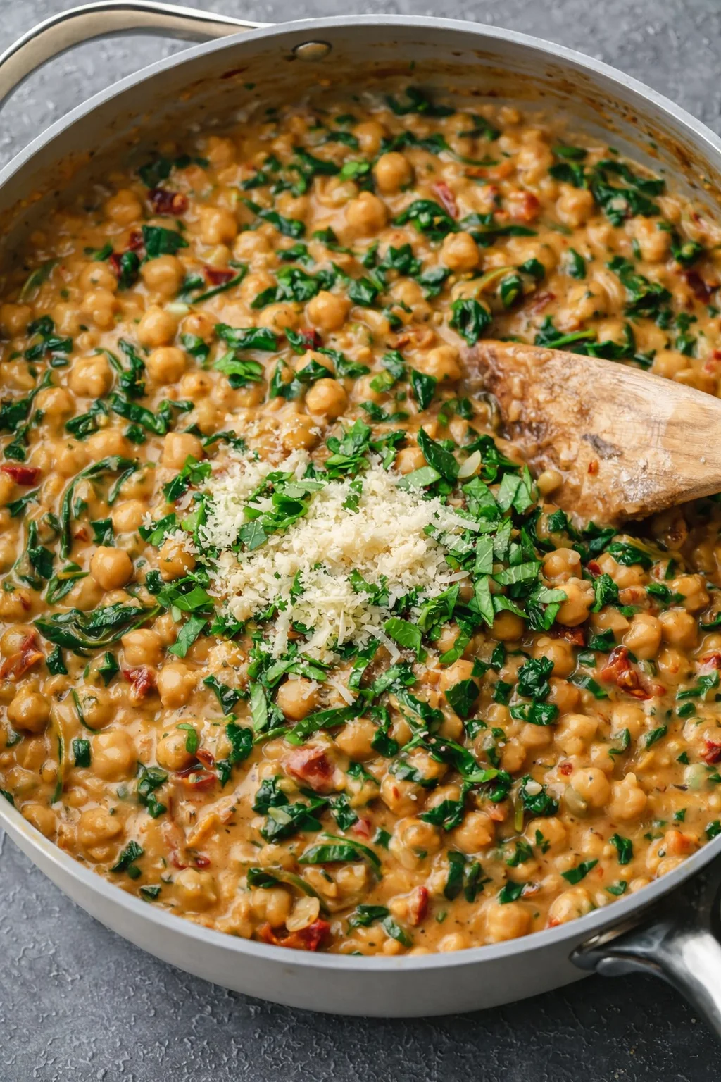 Creamy simmered chickpeas and wilted spinach in skillet, finished with chopped basil and vegan parmesan.