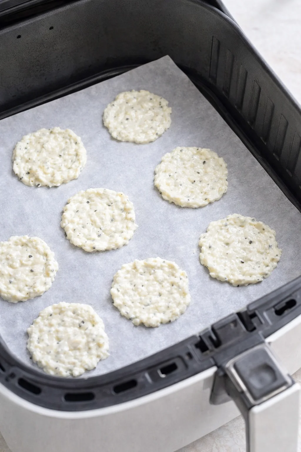 Uncooked sesame-speckled patties arranged on parchment in an air fryer basket.
