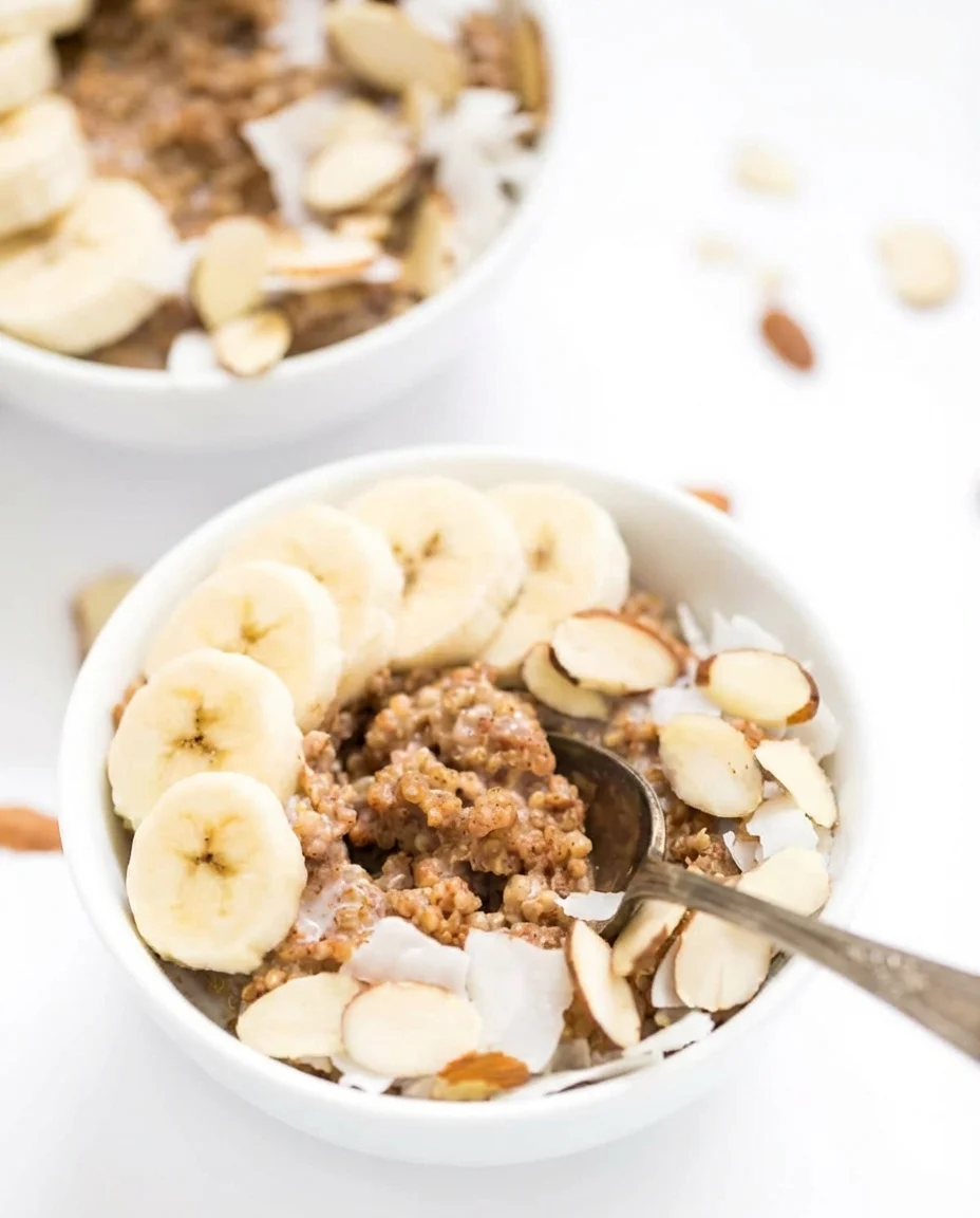 almond-quinoa-power-breakfast-4.jpg White bowl of yogurt topped with granola, sliced bananas, almond flakes, and coconut shavings.