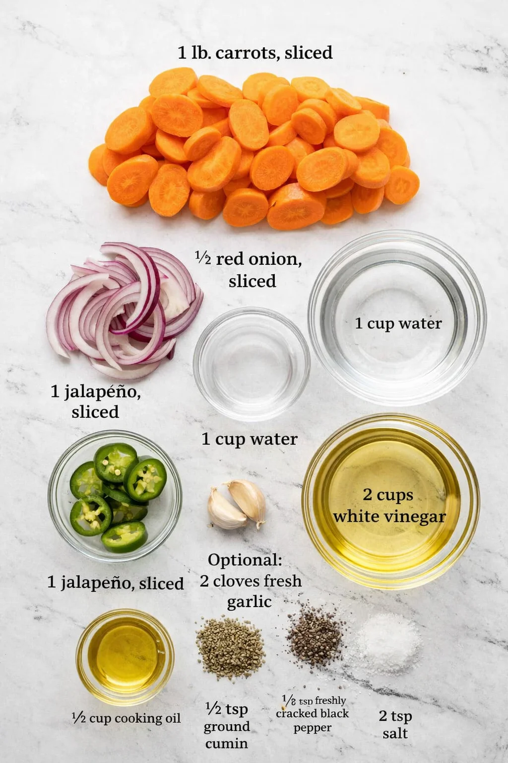 Overhead view of carrot slices, red onion, jalapeños, and bowls of water, vinegar, and oil for pickling.