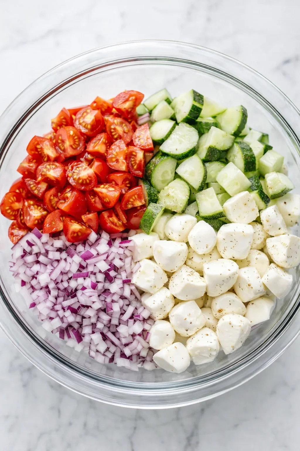 Medium bowl containing quartered cherry tomatoes, finely chopped red onion, and bite-sized mozzarella pieces.