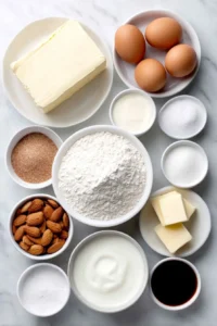 Flat lay of a block of softened cream cheese, slices of unsalted butter, two brown eggs with clean shells, a small mound of sugar crystals, a simple white ceramic bowl of cake flour, a small white bowl holding baking powder, another small white bowl with baking soda, a tiny white bowl of salt, a white bowl of buttermilk, a small white bowl with clear vegetable oil, a few whole almonds, a small white bowl of seedless raspberry jam with fresh raspberries nearby, a small white bowl of heavy cream, a small white bowl of confectioners sugar, and a small white bowl of vanilla extract, all arranged symmetrically and naturally on a clean white marble surface, soft natural light, photo taken with an iPhone, professional food photography style, fresh ingredients, white ceramic bowls, no bottles, no duplicates, no utensils, no packaging --ar 2:3 --v 7 --p m7354615311229779997 - Almond Raspberry Swirl Layer Cake, raspberry layer cake, almond dessert, layered berry cake, easy fruit layer cake
