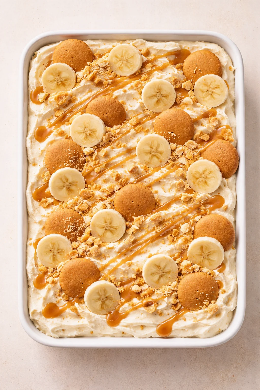 top-down view of banana pudding in a white baking dish, topped with banana slices and vanilla wafers