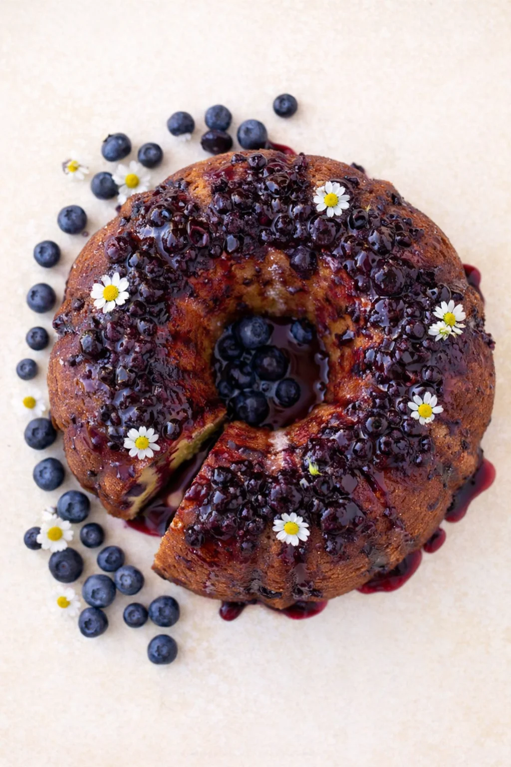 Bundt cake with blueberry glaze, fresh blueberries, and small white daisies as decoration.