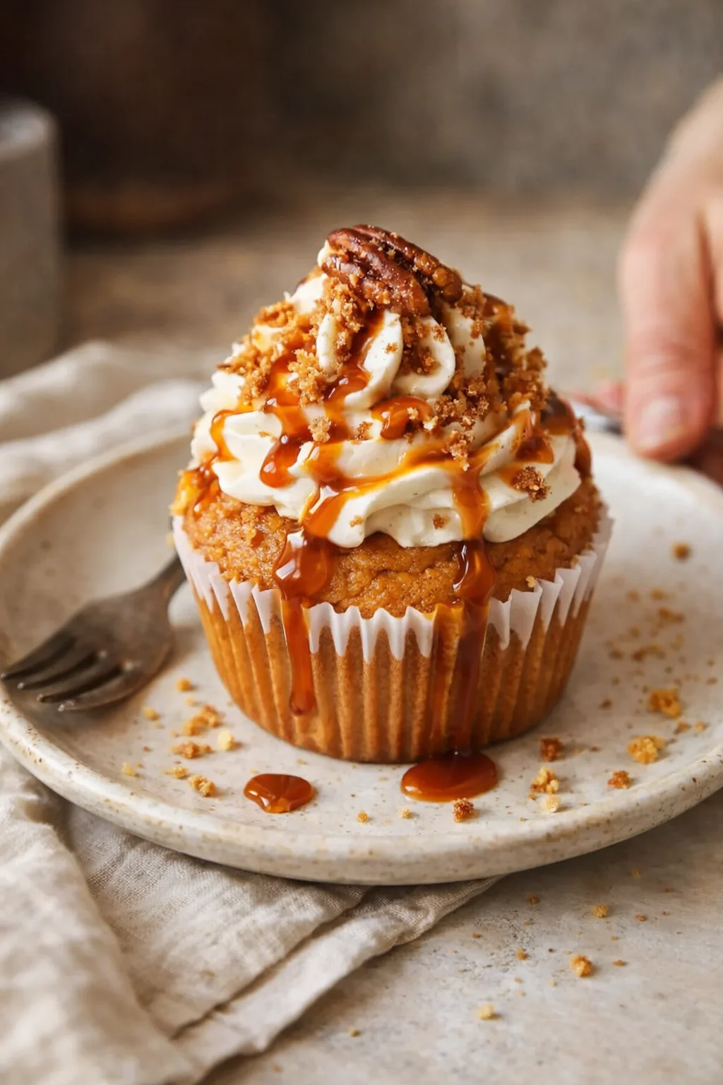 A caramel-drizzled cupcake with whipped cream frosting and crumbles on a plate.