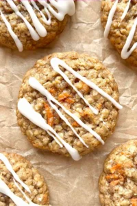 Carrot cake oatmeal cookies with cream cheese glaze scattered on a brown piece of parchment paper.