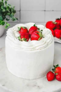 Strawberry cream cake on serving plate with whipped cream and fresh strawberries