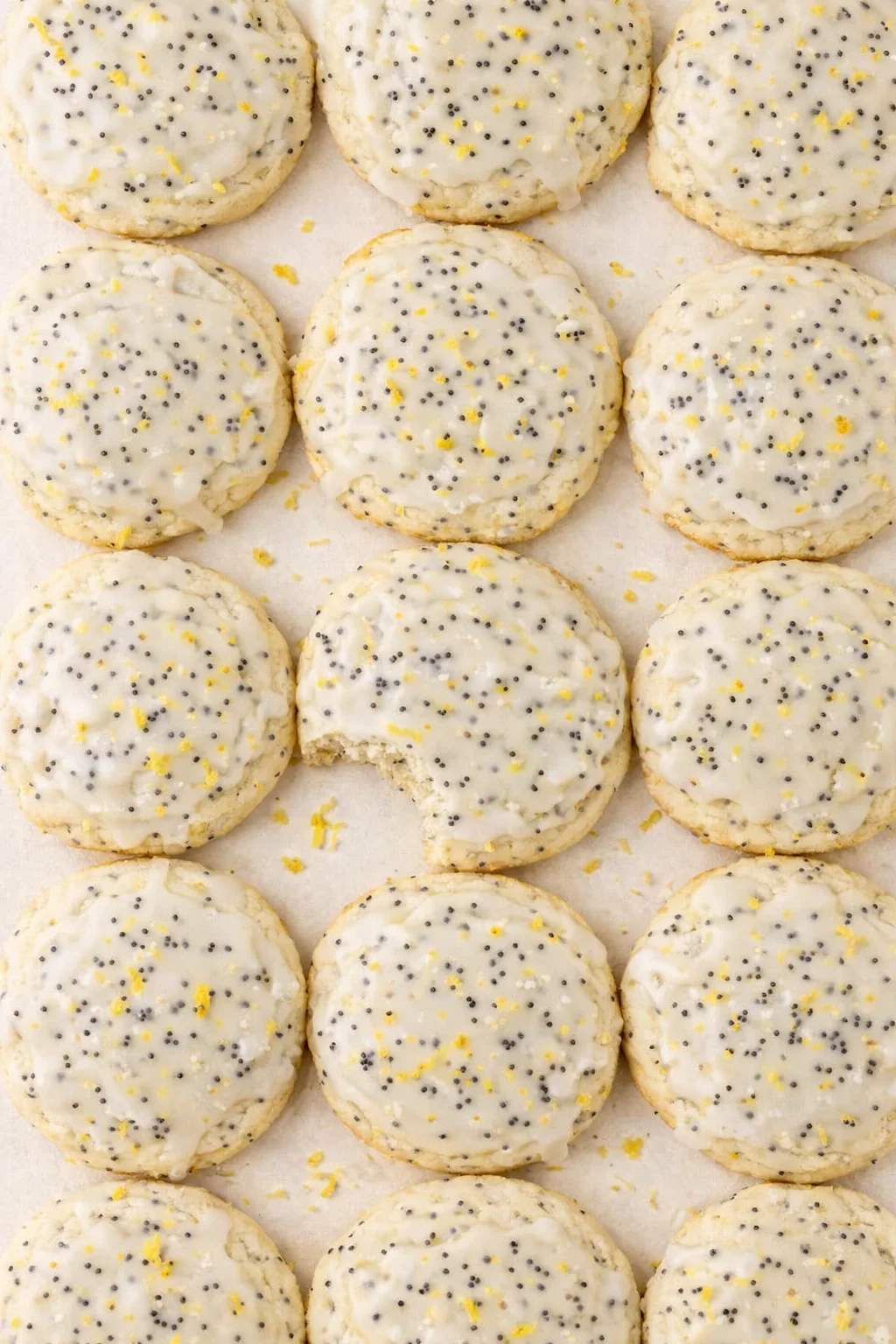 top-down view of lemon-glazed cookies speckled with poppy seeds on parchment