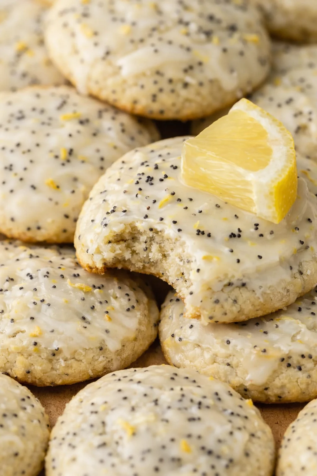 Close-up of lemon-glazed poppy seed cookies piled on a wooden board with a lemon wedge garnish