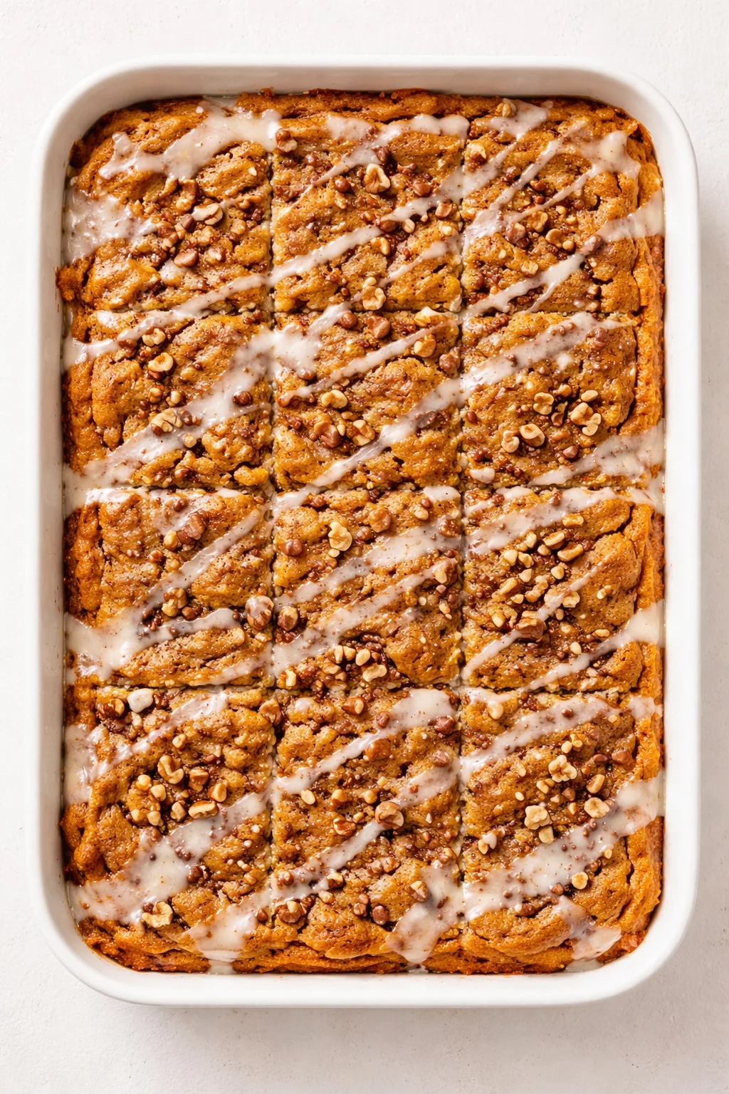 white baking dish filled with golden-brown cinnamon rolls topped with glaze and chopped nuts