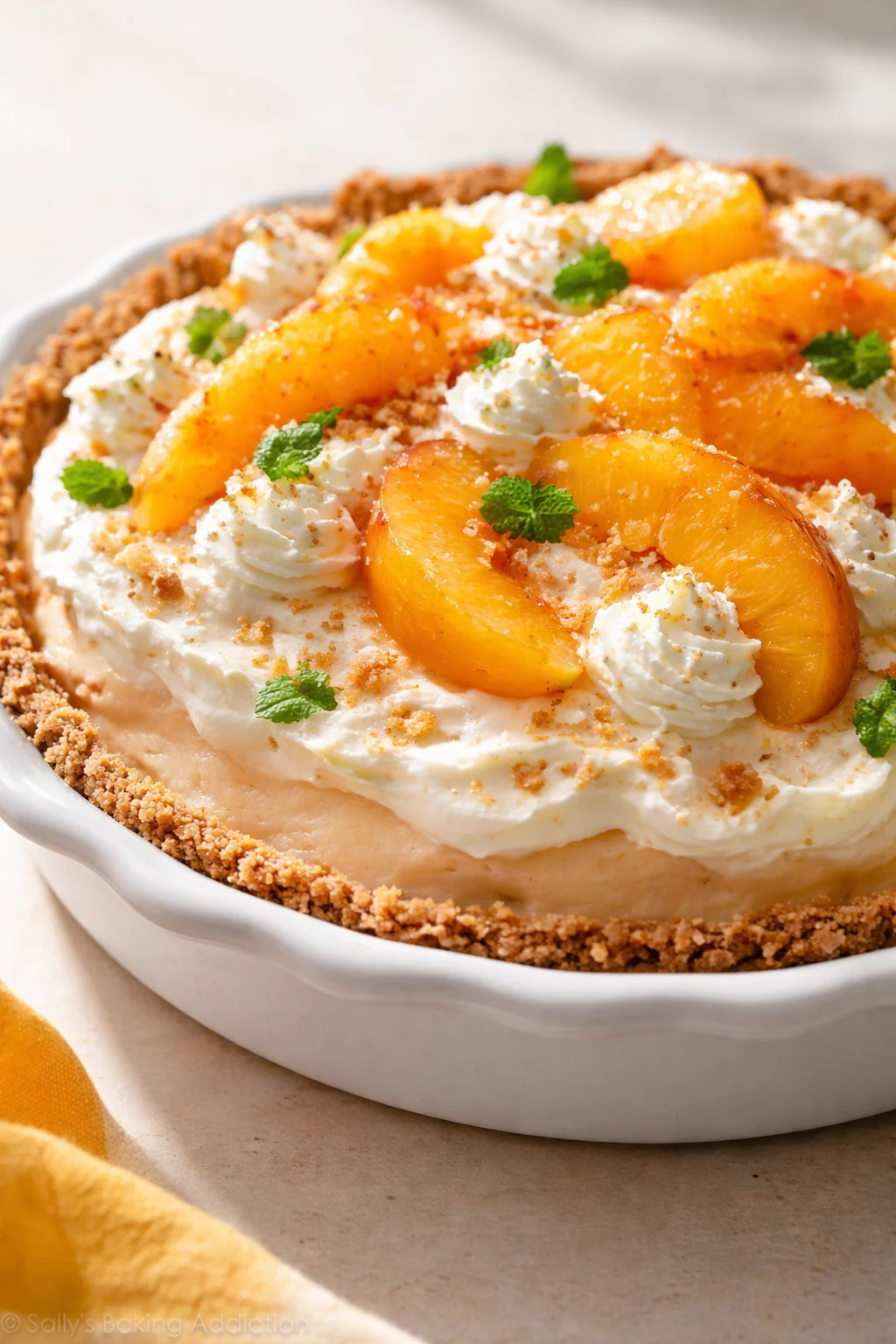 Peach slices arranged on whipped-cream topping over a crumb-crust pie in a white dish.
