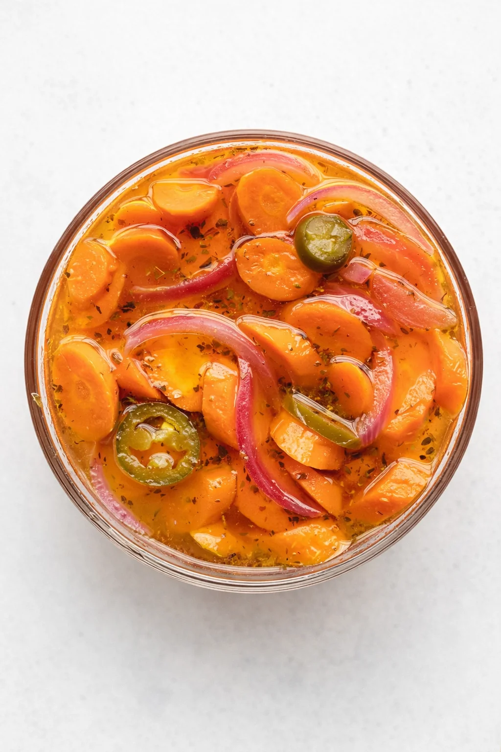 top-down view of a glass jar filled with orange carrot rounds, red onion slices, and green jalapeño slices in brine