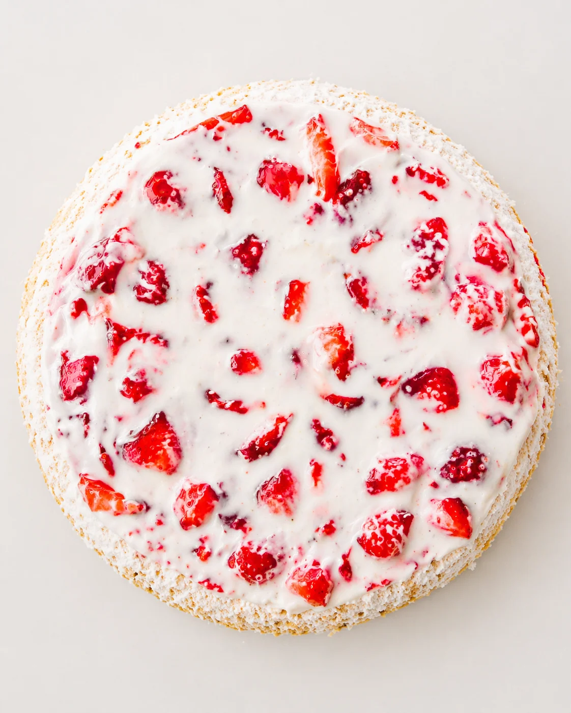 round cheesecake with a crumb crust, white creamy topping, and scattered red strawberries