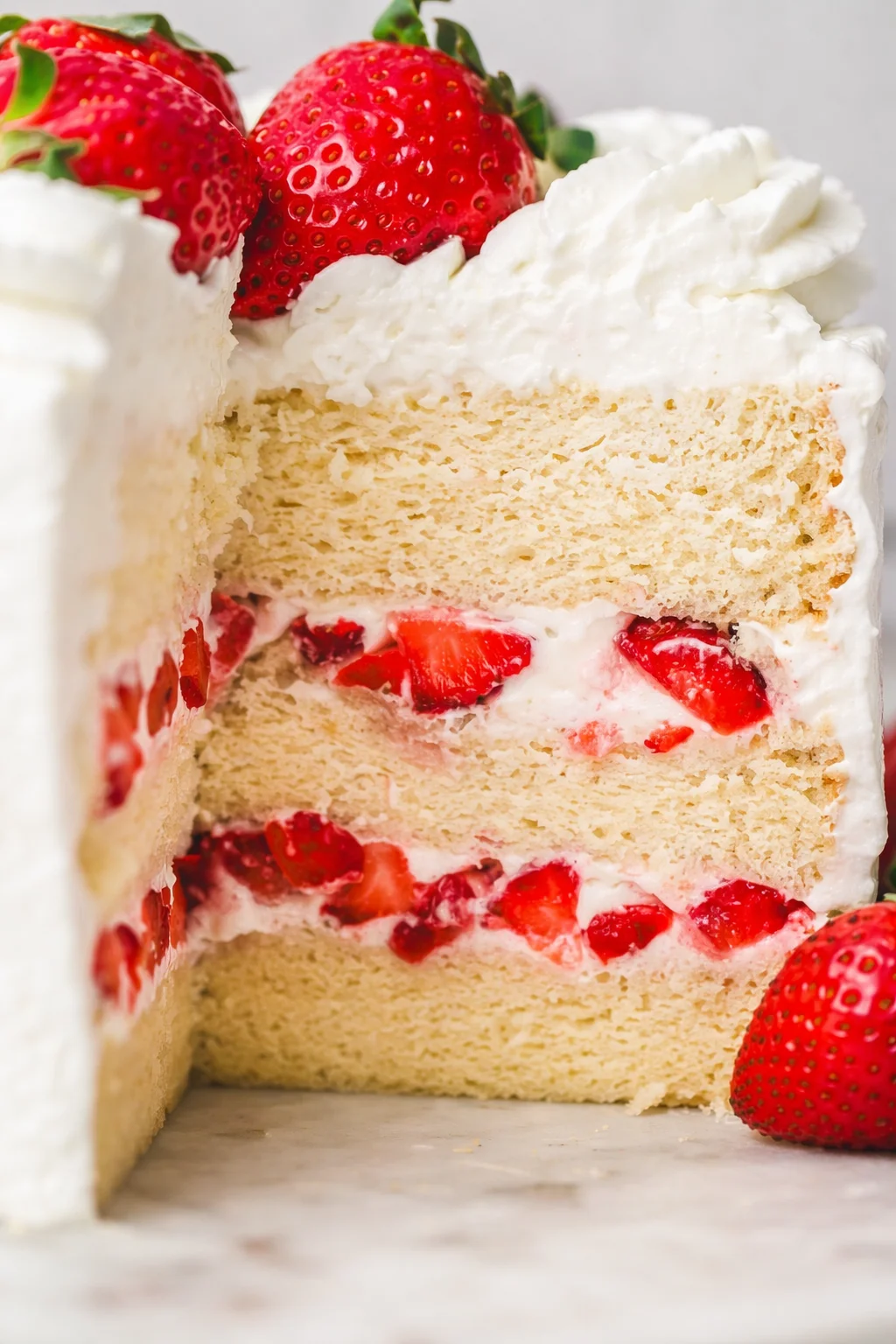 Close-up of a vanilla sponge cake with strawberry cream filling and fresh berries on top.