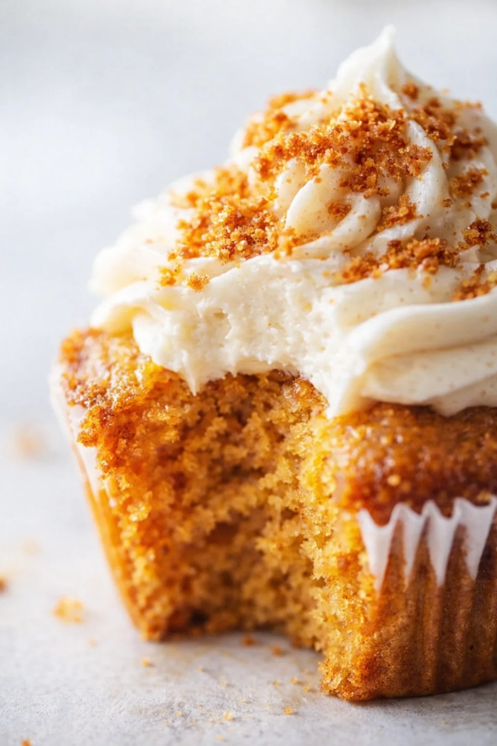 Close-up of a vanilla cupcake with white frosting and golden crumb topping.