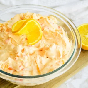 Closeup of bowl of mandarin orange jello salad on a wooden cutting board.