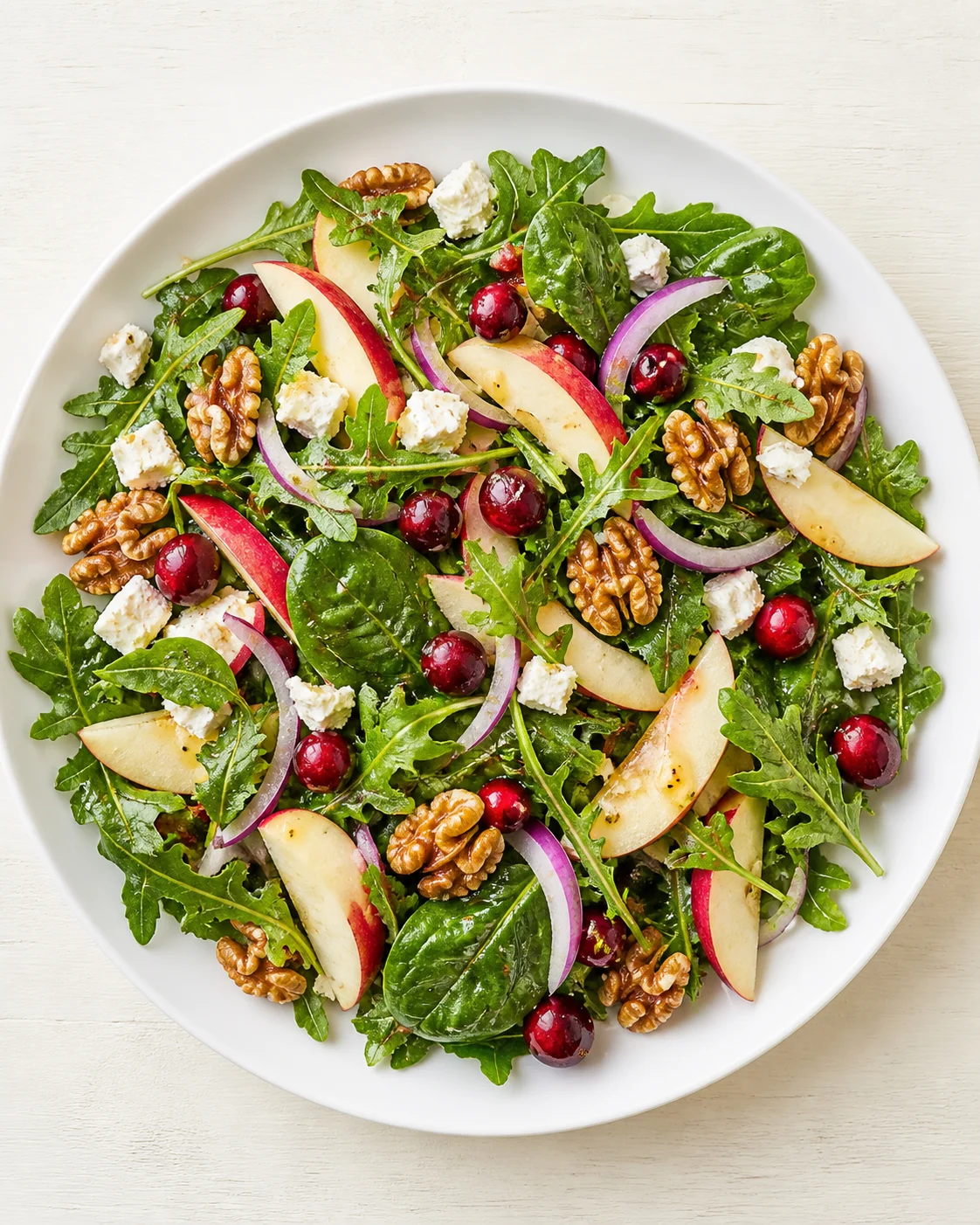 Top-down view of arugula salad with apple slices, walnuts, cranberries, red onion, and feta.