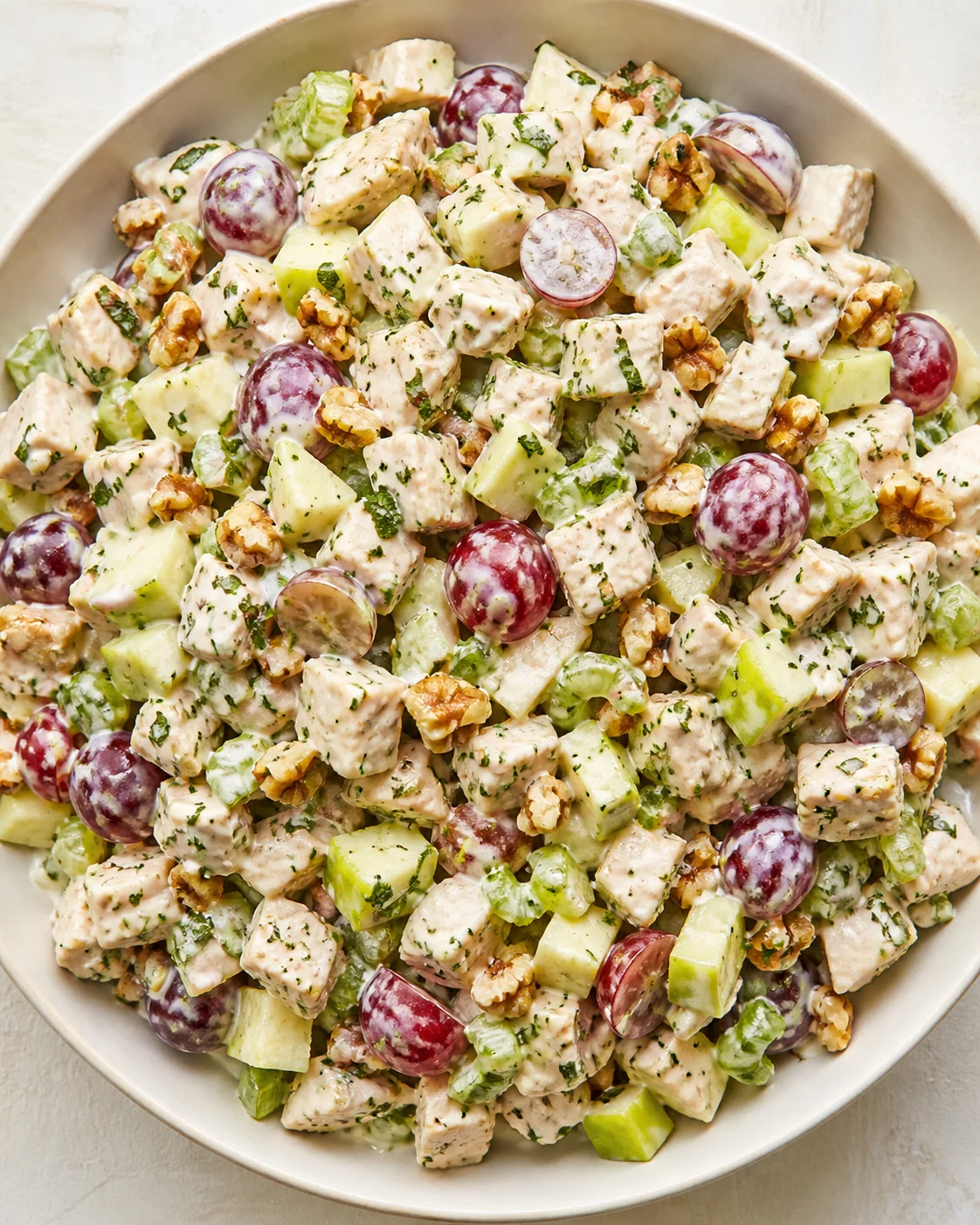Creamy chicken salad with grapes, walnuts, and diced celery in a light bowl