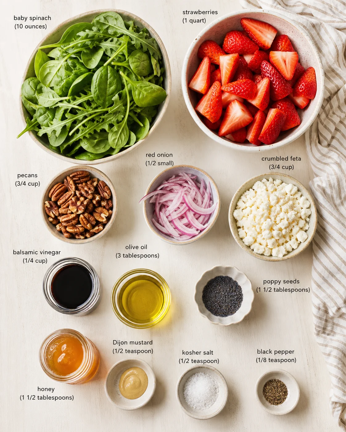 Overhead view of bowls with spinach, strawberries, feta, onions, pecans, oils, and spices labeled for a salad.