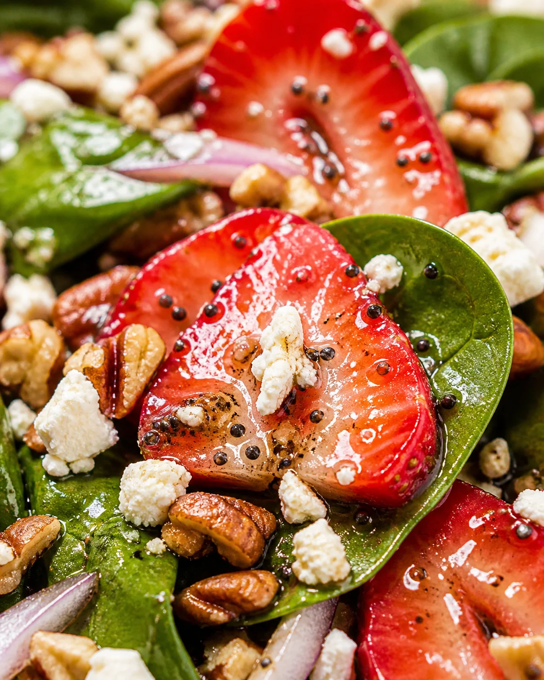 Close-up of a strawberry-spinach salad with feta cheese, pecans, and red onion.