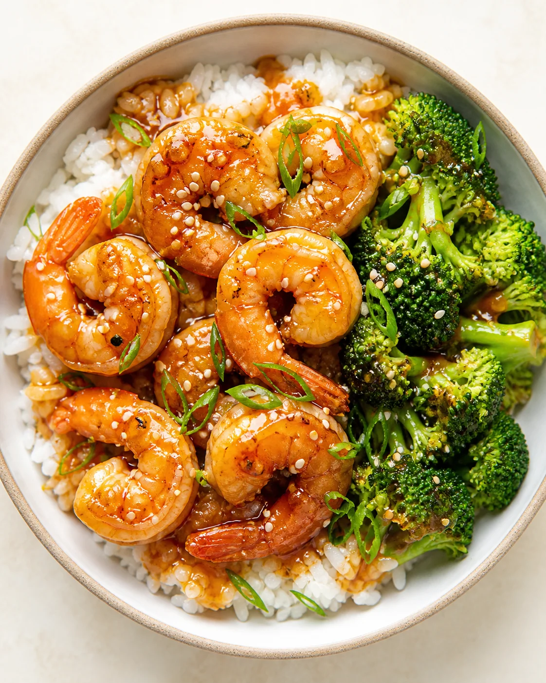 bowl of white rice topped with glazed shrimp, broccoli, sesame seeds, and scallions
