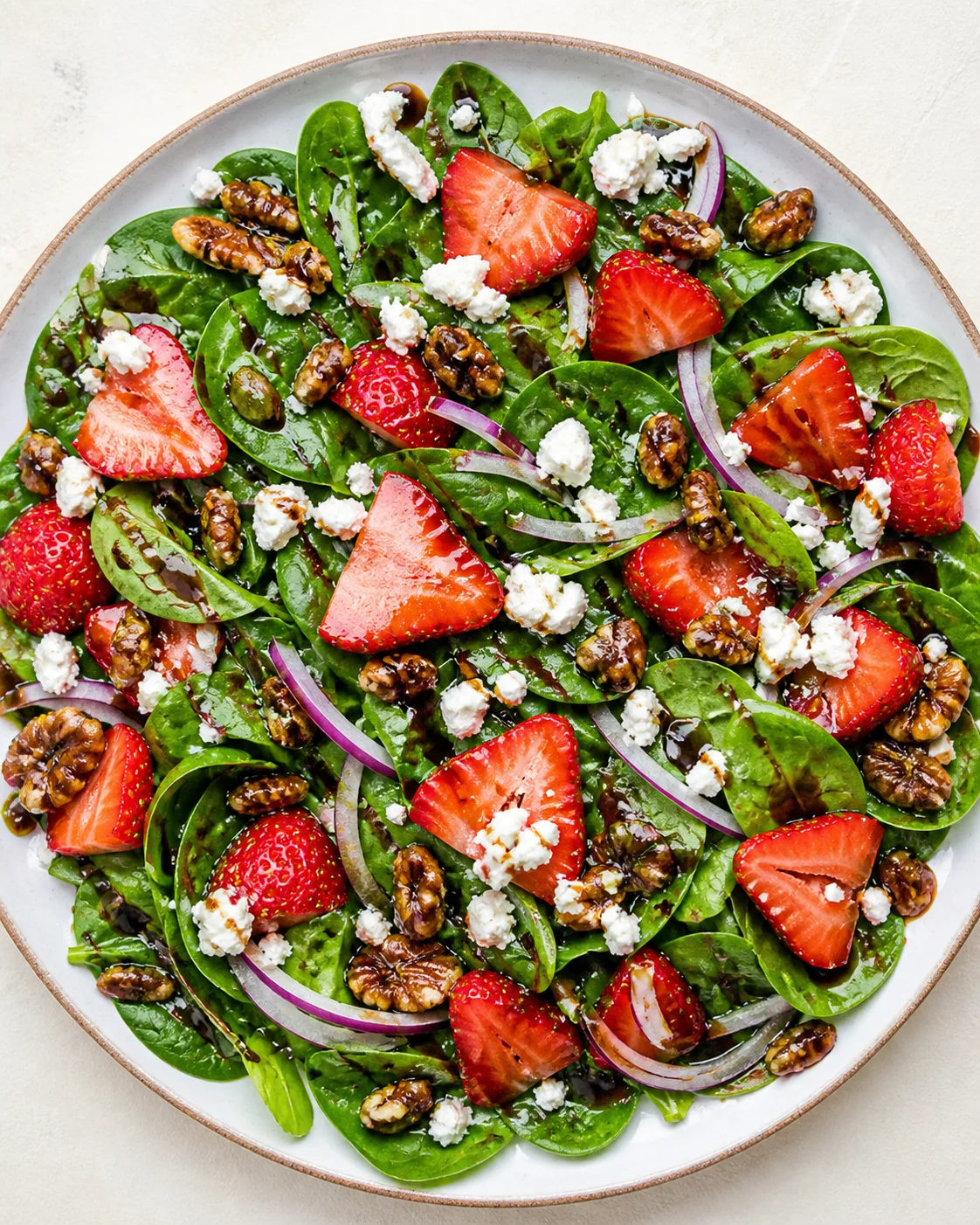 Bright plate of spinach salad topped with strawberries, walnuts, red onion, and feta with balsamic glaze.