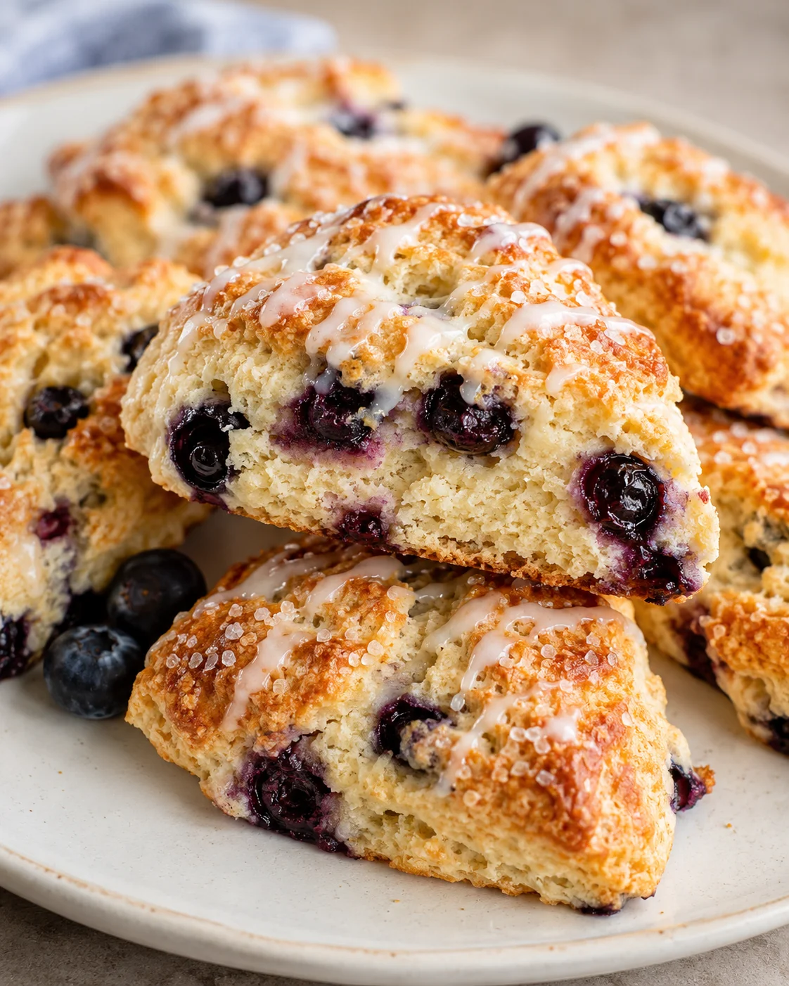 Close-up of freshly baked blueberry scones with glaze and berries on a plate
