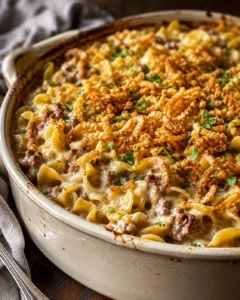 Creamy beef and pasta bake topped with crispy fried onions in a beige casserole.